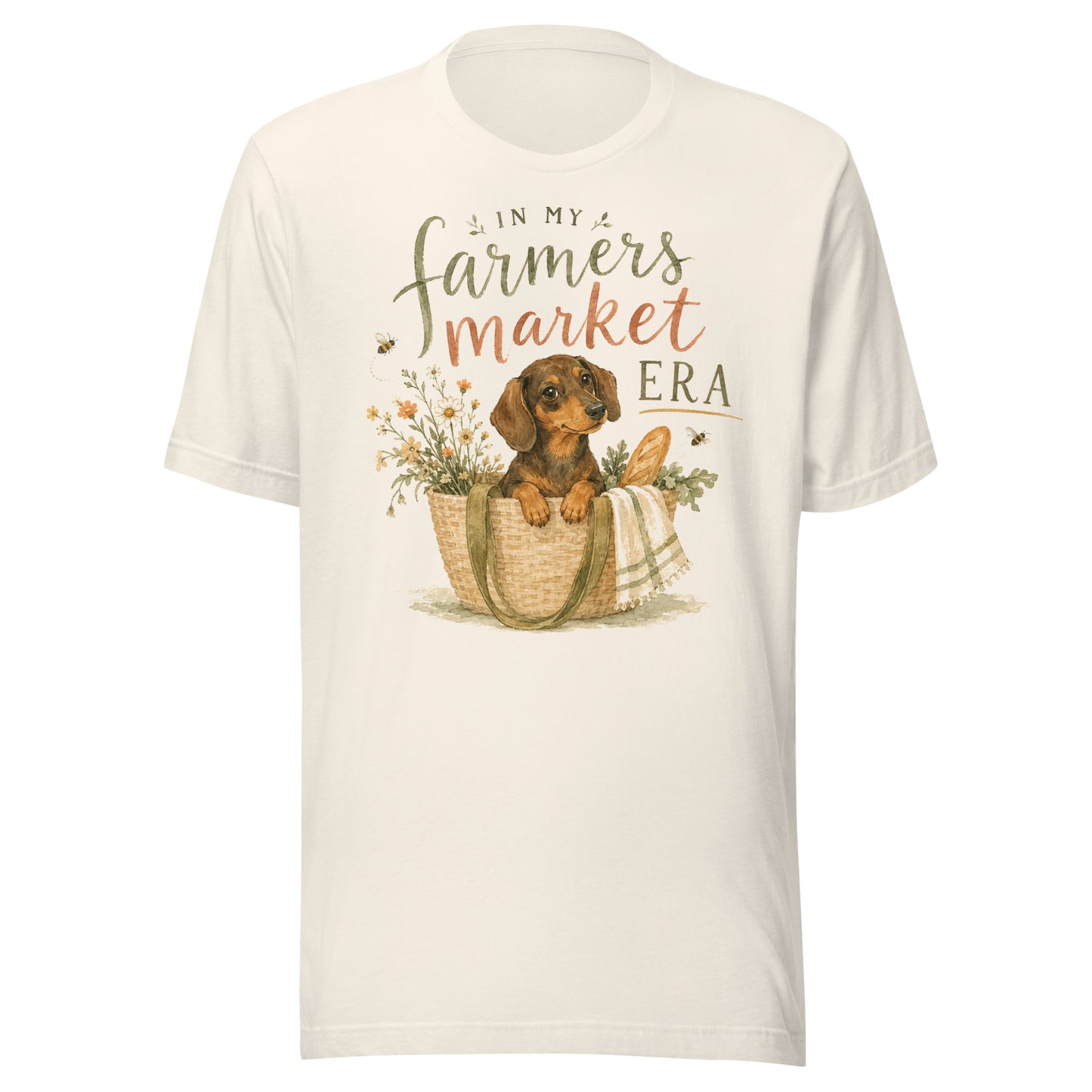 Cream unisex t-shirt reading In My Farmers Market Era with a watercolor illustration of a dachshund puppy in a market tote basket with flowers and bread
